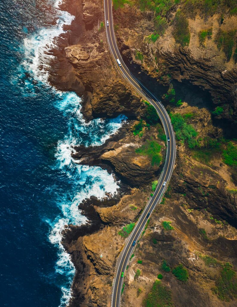 Stunning aerial shot of a winding coastal road in Hawaii with vibrant ocean waves.